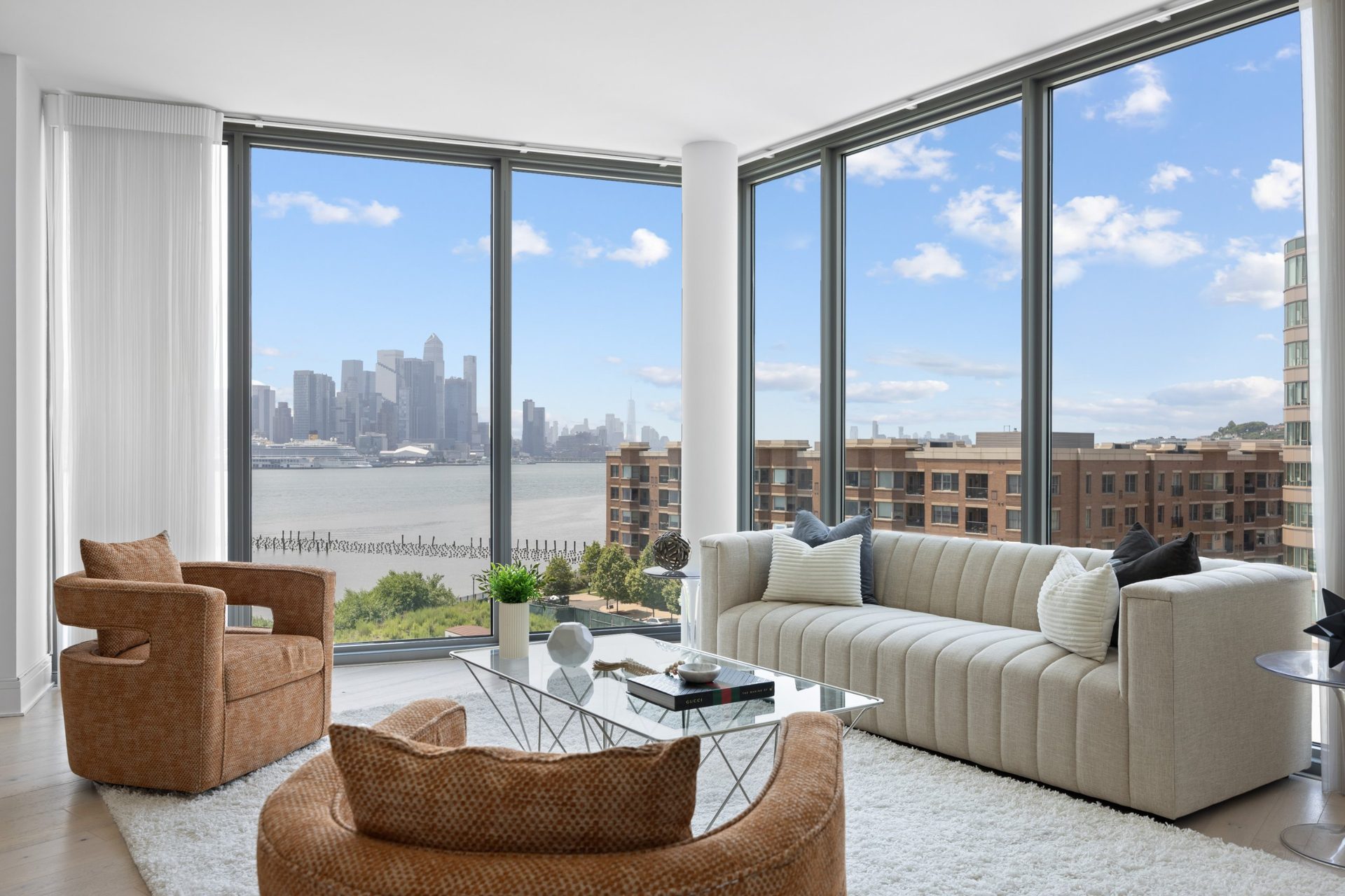 Sunlit living room with floor-to-ceiling windows overlooking the Hudson River and Manhattan